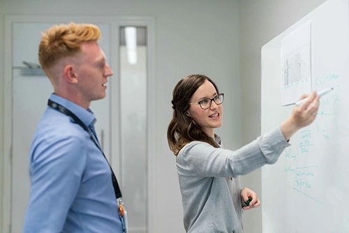 Projektmanagerin tauscht sich mit einem Kollegen ĂŒber die nĂ€chsten Schritte im Projekt aus Beratung und Software fĂŒr Digitalisierung und Industrie 4.0 sichern Ihre WettbewerbsfĂ€higkeit langfristig.